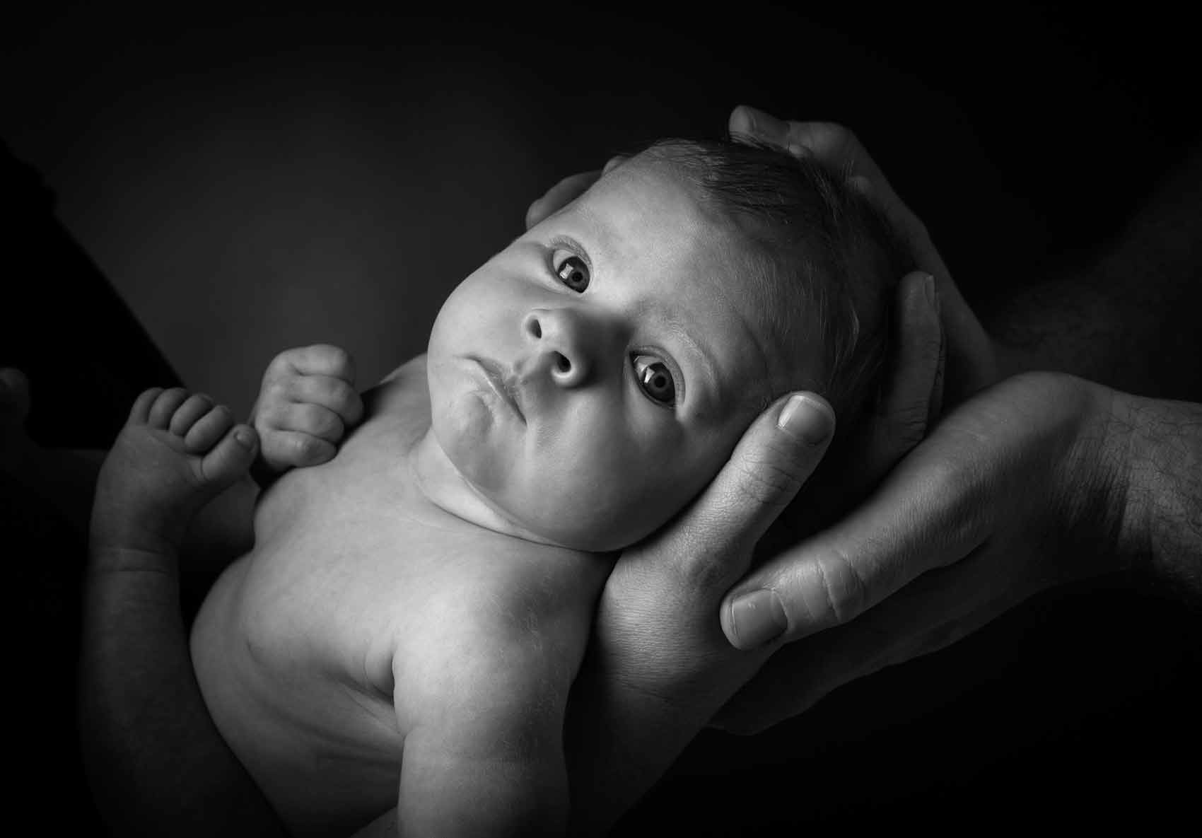 Portrætfoto af baby i mor og fars hænder